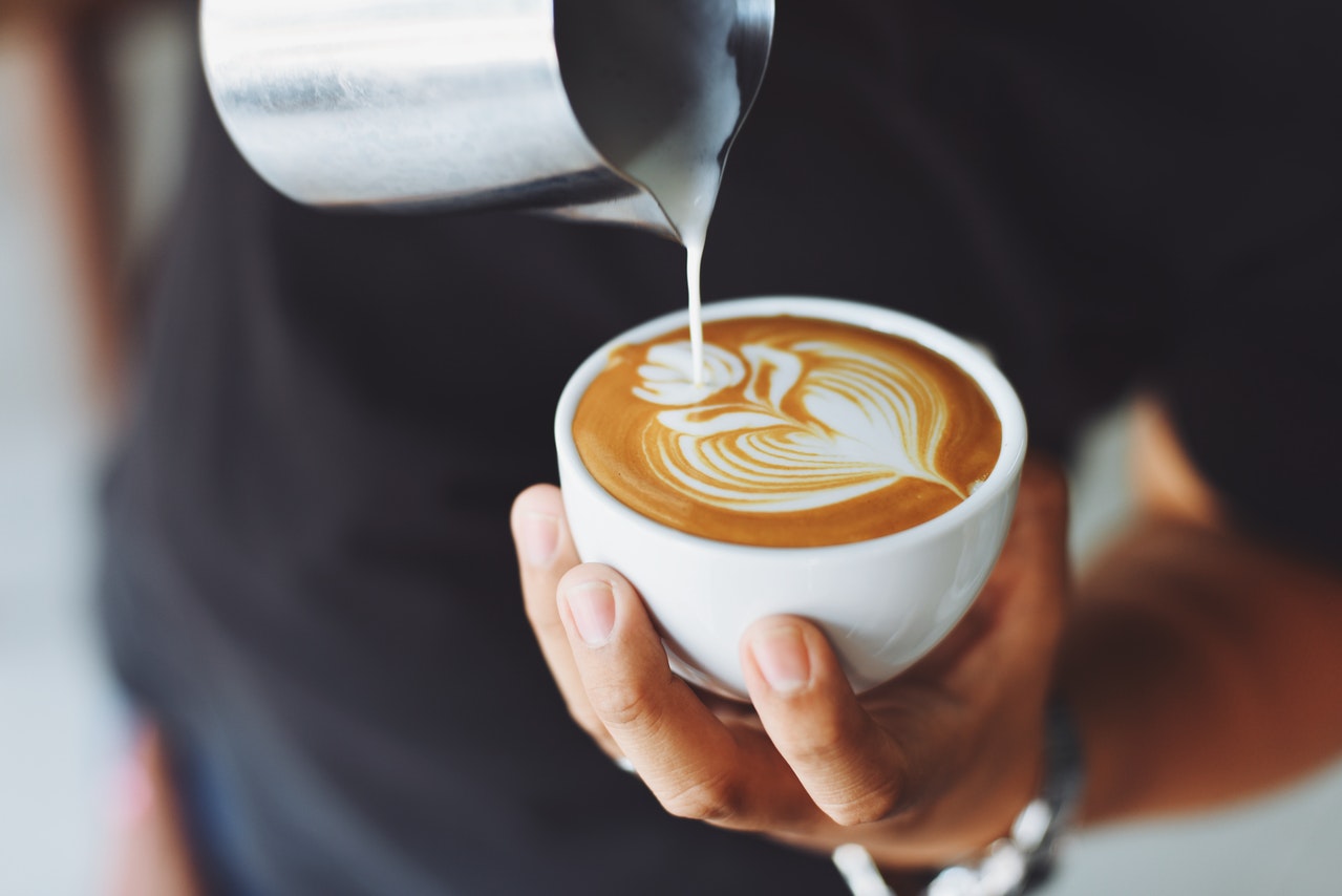person pouring milk into coffee cup