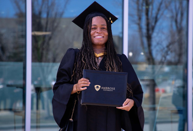 young woman wearing black robes and mortarboard hat, holding diploma in her hand. She is smiling